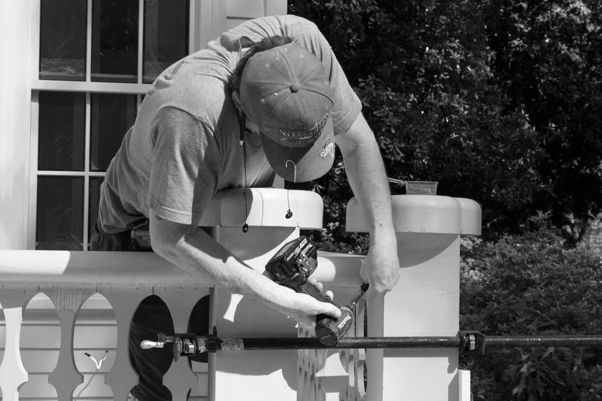 A home building professional leans over a new deck rail to drill in fastener holes.